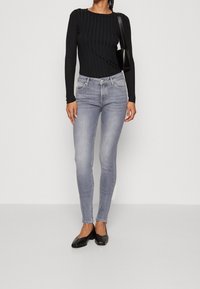 Top negro de manga larga acanalado combinado con jeans ajustados gris claro. Los zapatos son planos negros. La apariencia general es ajustada y casual.