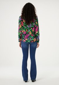 Blouse met lange mouwen met een multicolor bloemmotief op een donkere achtergrond, gecombineerd met wijde blauwe jeans en enkellaarsjes.