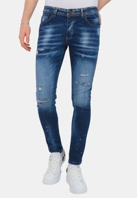 Slim-fit blauwe spijkerbroek met vervaagde delen, versleten patches en lichte vlekjes. Heeft een klassieke vijf-pocket ontwerp en riemlussen.