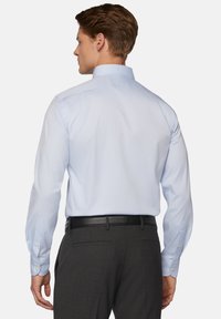 Svetlomodrá košeľa s dlhým rukávom, klasickým golierom, hladkou textúrou a zapínaním na gombíky, skombinovaná s tmavozelenými nohavicami a čiernym opaskom.