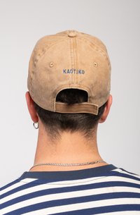 Căciulă din țesătură kaki cu curea de ajustare la spate, având brodat textul albastru "KAOTIKO." Design simplu cu un vârf rotunjit și textură moale.