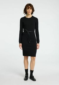 Robe noire à manches longues avec une silhouette ajustée et un détail de ceinture nouée à la taille ; fabriquée dans un tissu lisse et extensible.