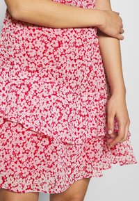 Blommönstrad klänning med lager i nyanser av rosa och röd, tillverkad av lättviktig tyg med en mjuk, strukturerad yta.