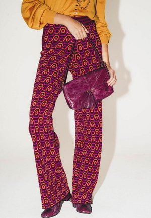 Pantaloni viola con fantasia a esagoni in arancione e rosa. Abbinati a una borsa bordeaux dalla trama evidente e scarpe coordinate.