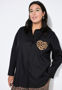 Black button-up shirt with a leopard print heart pocket. Features long sleeves and a relaxed fit. Smooth, lightweight fabric.