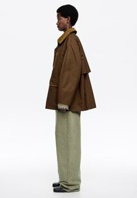 Hnedá prešívaná bunda s jemne rybkovitou golierom, skombinovaná so svetlozelenými širokými nohavicami. Bunda má gombíkové detaily a voľný strih.