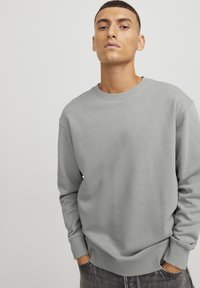 Sudadera gris claro de algodón con textura acanalada, cuello redondo y mangas de puño, combinada con jeans de mezclilla oscura.