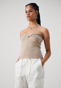 Beige strapless tops ar ar virsotni ar mezgla priekšpusi, izgatavoti no ribota auduma. Uzvilkti kopā ar baltām kravas biksēm, kurām ir sānu kabatas.