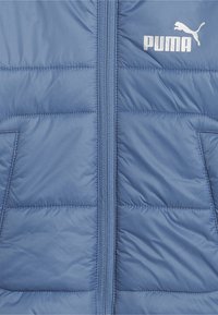 Blå puffy väst gjord av slätt, kviltat material. Har en framsida med dragkedja, två sidofickor och en vit Puma-logotyp på bröstet.