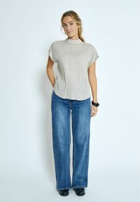 Kurzärmliges Oberteil mit hohem Kragen in Creme mit vertikalen Streifen und kleinen Punkten, kombiniert mit weiten blauen Jeans und schwarzen Schuhen.