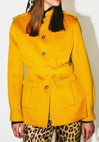 Veste militaire style jaune en mélange de laine avec deux poches avant, fermeture boutonnée, taille ceinturée et épaulettes.