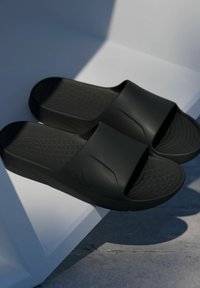 Black slide sandals made of durable rubber with a textured footbed, wide straps, and understated design. Features a subtle logo.