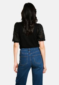 Zwarte top met gestructureerde kantmouwen, gecombineerd met hooggetailleerde denim jeans met achterzakken in een klassieke blauwe kleur.