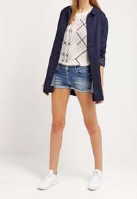 Námořnická košile na knoflíky přes bílý vzorovaný top, doplněná džínovými kraťasy a bílými teniskami. Hladká látka, volný střih, ležérní styl.