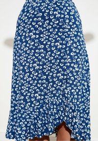 Jupe plissée bleue ornée d'un motif floral blanc, avec un ourlet volanté et un tissu texturé. Le design comprend des motifs de feuilles délicats tout au long.