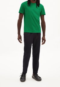 Zelené bavlněné tričko s krátkými rukávy, spárované s tmavě námořnickými kalhotami. Obuv má černý tvarovaný design s výřezy.