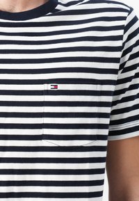 Navy and white striped t-shirt with a round neckline, patch pocket, and small logo accent. Cotton fabric with a soft texture.