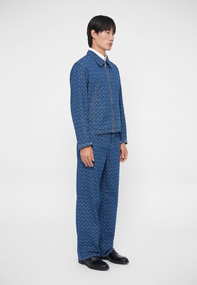 Conjunto de chaqueta y pantalones de mezclilla azul con un patrón sutil, cremallera frontal y grandes bolsillos. La tela tiene una textura suave.
