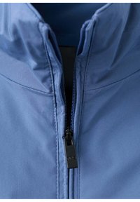 Gros plan d'une veste bleue partiellement zippée avec le curseur de fermeture éclair visible et des détails de couture le long du col et de la couture frontale.