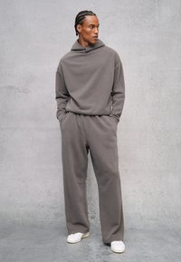 Felpa con cappuccio grigia e pantaloni jogger in tessuto morbido, con vestibilità rilassata. L'outfit presenta tasche laterali e dettagli di design semplici.