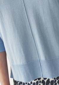 Maglione lavorato a maglia azzurro chiaro con vestibilità ampia, caratterizzato da un orlo a coste e una finitura testurizzata. Una cucitura decorativa corre lungo il centro della schiena.