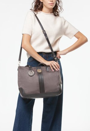 Borsa in tessuto grigio con dettagli in pelle nera, doppi manici superiori, tracolla regolabile e un medaglione decorativo in metallo con logo.