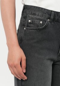 Sorte denim jeans med høy midje, front- og baklommer med sølvnitter, og et teksturert stoff for en slitesterk finish.