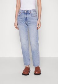 Světle modré džíny z denimu se střihem rovného nohavice, pěti kapsami a jemnými vintage prvky. Kombinované s hnědými dřeváky, které mají zaoblenou špičku.