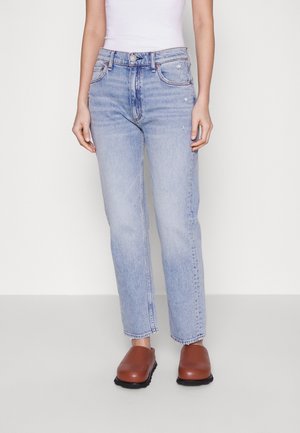Jeans de mezclilla azul claro con corte recto, cinco bolsillos y detalles de desgaste sutiles. Llevados con zuecos marrones, con una parte frontal redondeada.