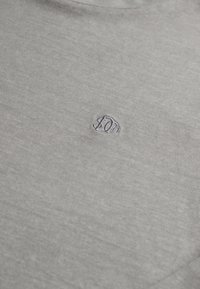 Graues T-Shirt aus weichem Stoff, mit einem kleinen gestickten Logo auf der linken Brustseite. Einfacher, runder Ausschnitt mit kurzen Ärmeln.
