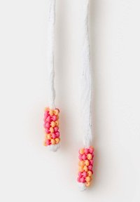 Lacets blancs avec des groupes cylindriques de perles roses et orange attachés près des extrémités, suspendus sur un fond blanc.