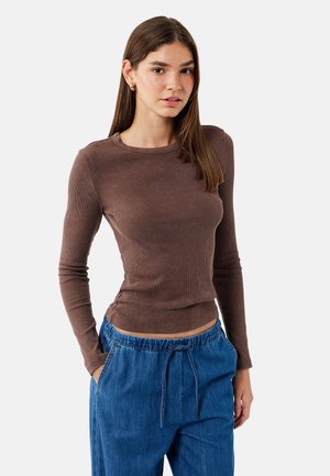 Langarm, geribbelde bruine top met een ronde hals, gecombineerd met losse blauwe broeken met een elastische tailleband en zijzakken.