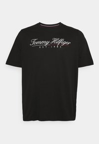 Černé bavlněné tričko s kulatým výstřihem a krátkými rukávy. Na přední straně je bílé logo "Tommy Hilfiger" a nápis "EST. 1985".