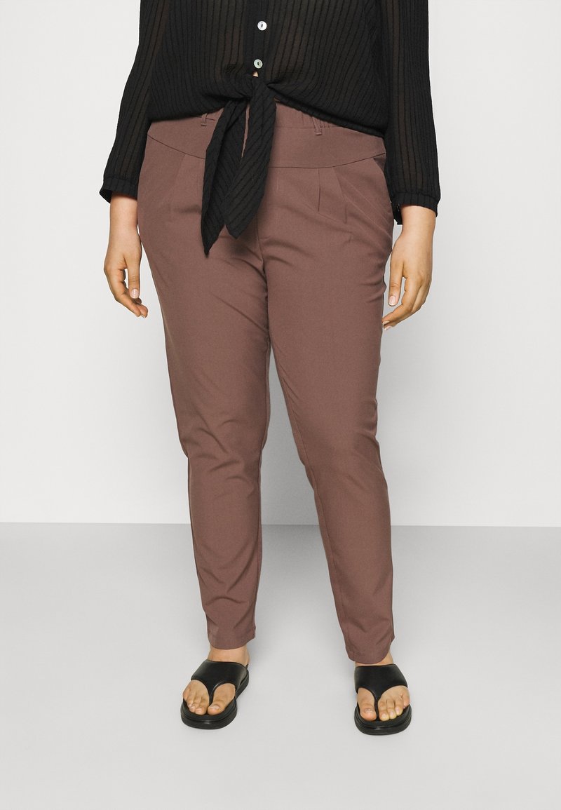 Pantalon marron coupe ajustée avec une texture lisse et des poches avant, associé à un haut noir côtelé à boutons, noué à la taille. Sandales noires portées.