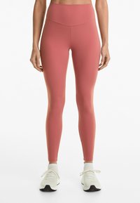 Höga, lätta leggings i en mjuk rosafärg, med en slät yta och en kroppsnära passform. Kombinationen kompletteras med vita sportskor.
