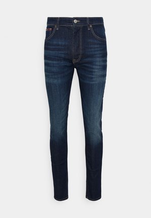 Dark blue denim jeans featuring a slim fit, five-pocket design, and contrasting golden stitching. Button closure at the waistband.