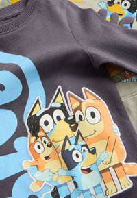 Gros plan d’une chemise grise avec une famille dessin animé colorée de quatre chiens souriants qui s’enlacent.