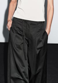 Black wide-leg trousers with a smooth texture, featuring a waistband, belt loops, front pleats, and side pockets.
