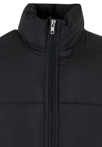 Doudoune noire matelassée avec un col haut, fermeture éclair à l'avant et détails de couture supplémentaires. Texture lisse et design minimal.