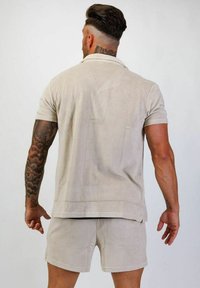 Beige kortärmad polo skjorta i mjukt tyg, matchande med shorts. Har en enkel design och kontrasterande sömnad.