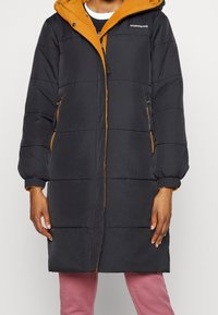 Abrigo acolchado negro con diseño bicolor, que presenta una capucha naranja y detalles de cremallera, patrones acolchados horizontales y puños elásticos.