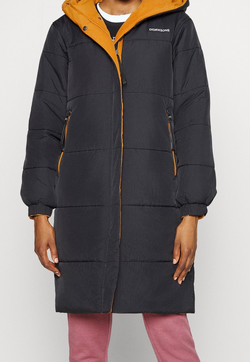 Abrigo acolchado negro con diseño bicolor, que presenta una capucha naranja y detalles de cremallera, patrones acolchados horizontales y puños elásticos.