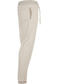 Lichtbeige joggingbroek van zacht materiaal, met een tailleband met trekkoord, een zijzak en taps toelopende pijpen met elastische boorden.