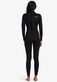 Muta nera con maniche lunghe, design aderente, materiale in neoprene liscio e cerniera posteriore. Presenta un dettaglio del logo sulla parte superiore della schiena.
