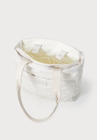 Sac fourre-tout blanc avec une texture lisse, doté de quincaillerie dorée, de deux longues poignées et d'un intérieur beige avec fermoir à pression.