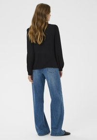 Sort langærmet bluse med samlede skuldre, parret med lyseblå viddejeans. Glat tekstur, enkelt design, ingen synlige mønstre.