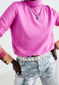 Sweter z golfem w kolorze fuksji, wykonany z miękkiego materiału. Srebrne metaliczne dżinsy o błyszczącej fakturze oraz biały pasek z czarnymi metalowymi elementami.