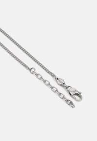 Cadena de metal plateado, con eslabones entrelazados, un cierre de langosta y una pequeña etiqueta grabada con "Fossil". Superficie suave con un acabado brillante.
