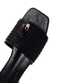 Sandal aperto neri con punta scoperta, dotati di una fascia intrecciata testurizzata e suola piatta. Presenta un dettaglio di chiusura in tono oro sulla fascia. Finitura liscia.