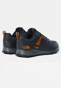 Paire de chaussures de randonnée The North Face bleu foncé et orange avec semelles texturées et col rembourré, vue de dos et de côté.